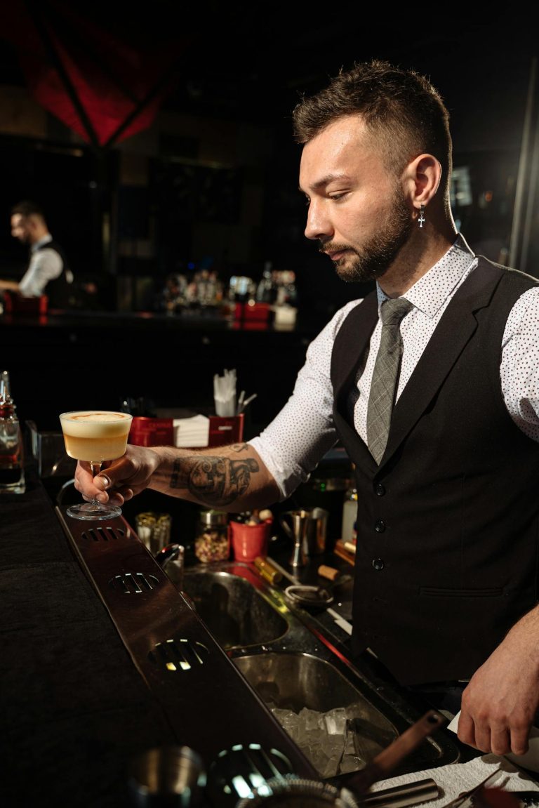 A skilled bartender with tattoos prepares a cocktail at an elegant bar.