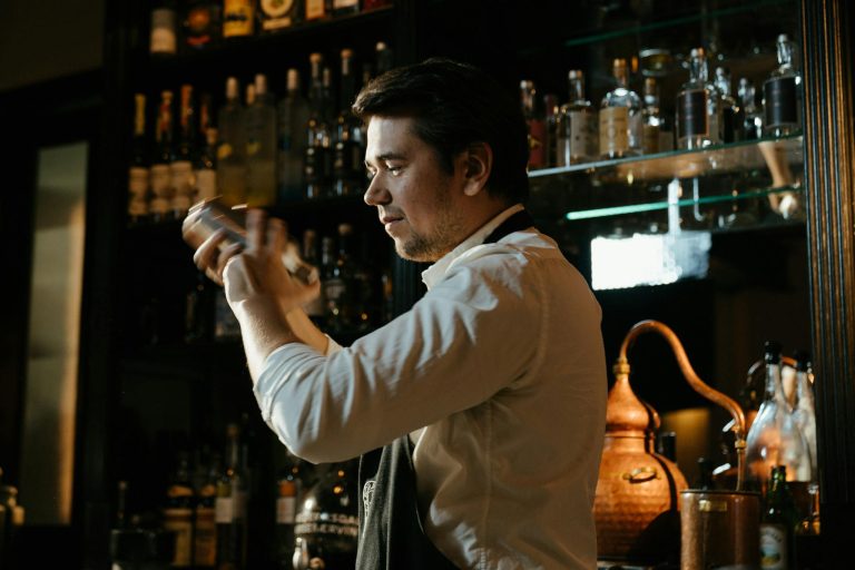 An experienced bartender skillfully shakes a cocktail in a cozy, warmly lit bar setting.