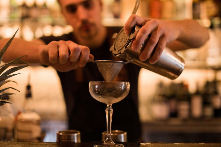 Bartender using a shaker and strainer to craft a cocktail at a dimly lit bar.